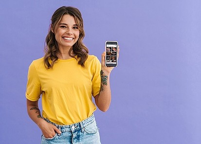 Eine Frau steht vor lila Hintergrund und zeigt ihr Smartphone mit der papperts App.